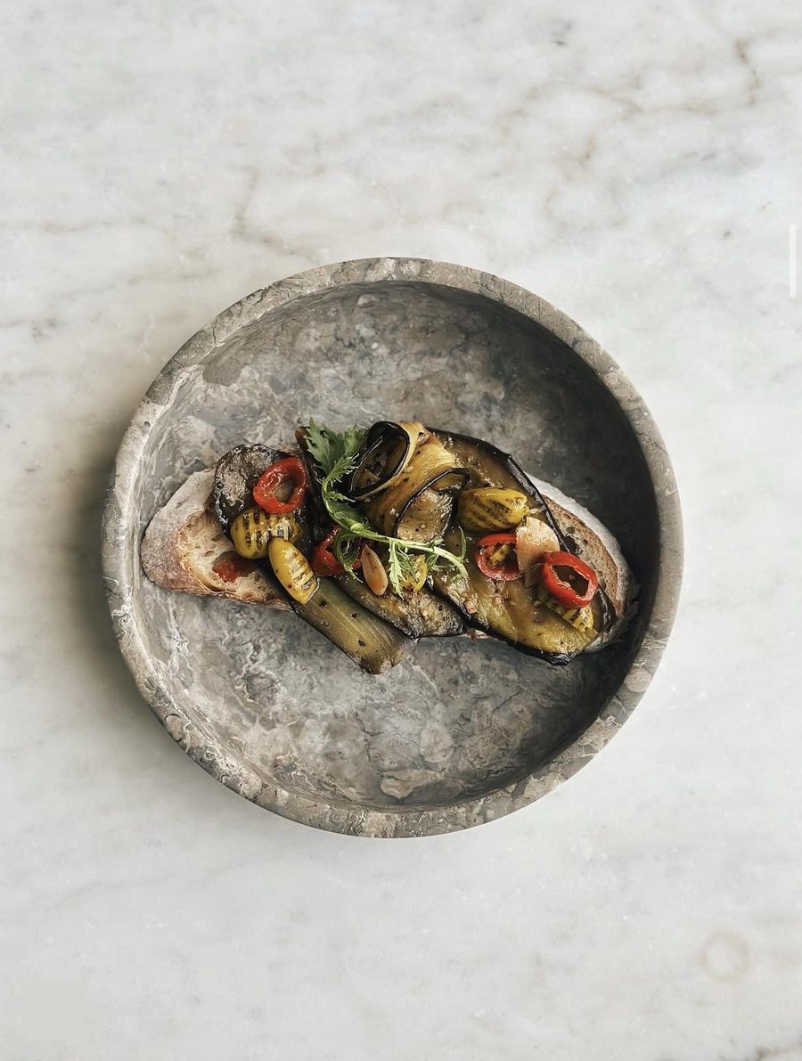 Sourdough toast topped with grilled aubergine, peppers and herbs in a stone bowl
