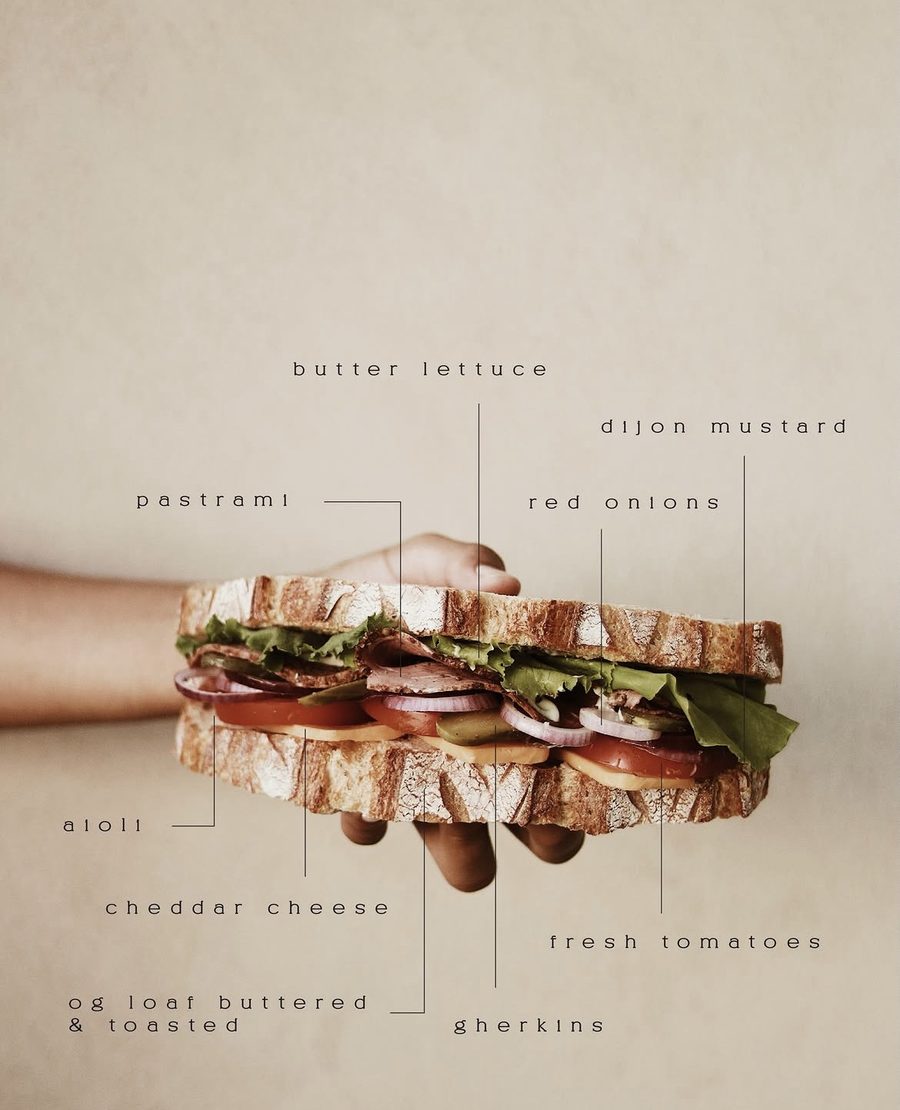 Stacked sourdough sandwich with pastrami, butter lettuce, cheddar, tomato, red onion and gherkins, ingredients labelled