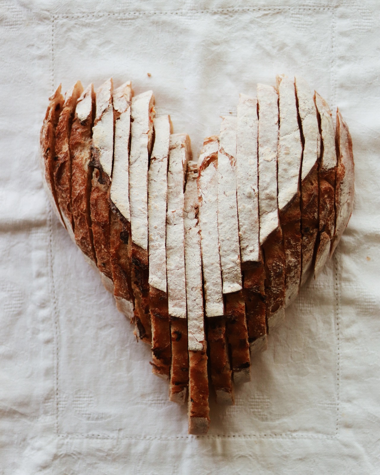 A whole sourdough loaf sliced and arranged into a heart shape on a white cloth